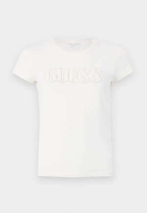 T-shirt blanc à manches courtes en coton, avec un logo "GUESS" en relief décoré de petites paillettes sur la poitrine.