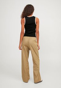 Top negro sin mangas con ribete blanco, combinado con pantalones beige sueltos. La tela parece suave, con una textura lisa y un ajuste relajado.