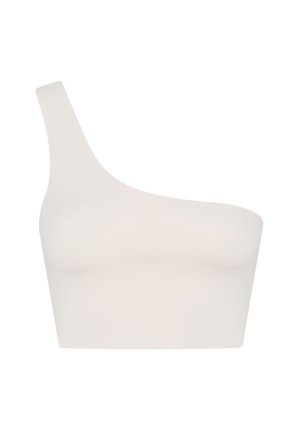 Frau in weißem Tanktop und schwarzer Hose, die in einem Handstand mit gebeugten Beinen auf einem schlichten hellen Hintergrund balanciert.