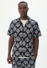 Camicia a maniche corte in tessuto blu navy con intricate fantasie floreali bianche, colletto a punte e chiusura frontale con bottoni.