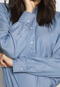 Light blue denim shirt featuring a button-up front, long sleeves with gathered cuffs, and subtle texture. Soft fabric with classic design.