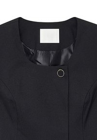 Zwarte jas met een gladde stofafwerking, ronde halslijn en een zichtbare logo-label. Voorzien van een gouden ronde sluiting aan de voorkant.