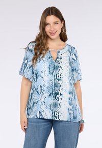 Top con stampa serpente blu, maniche corte, scollo a chiave e tessuto morbido. Abbinato a jeans in denim dal taglio comodo.