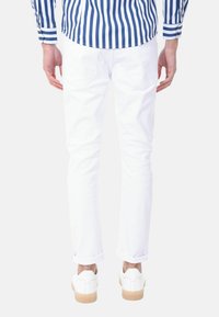 Jeans bianchi a taglio slim, con risvolti, abbinati a sneakers bianche. La camicia ha righe verticali blu navy e maniche lunghe.