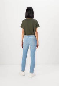 Jean slim en denim bleu clair associé à un t-shirt vert foncé. Les jeans sont dotés d'une taille standard et de poches arrière.