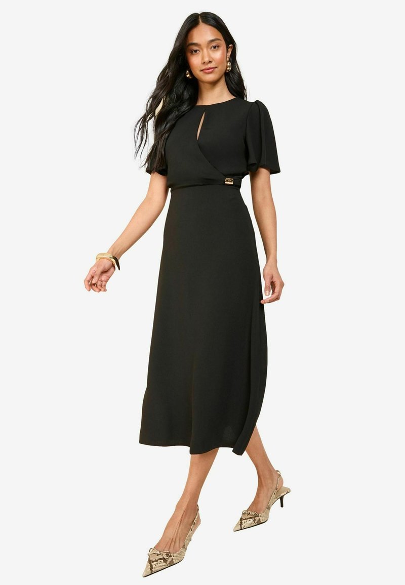 Vestido midi negro con mangas cortas tipo globo, detalle de ojal en el escote y un acento dorado en la cintura. Tela suave y diseño fluido.