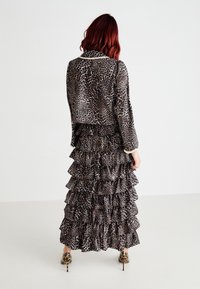Leopardmønstret bluse og tieret maxi-nederdel med rynkede lag. Mørk og lys brun farver, gennemsigtigt stof og højhælede sko.