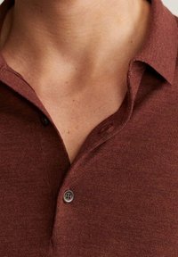Polo shirt bordeaux con colletto a bottoni, caratterizzato da una texture morbida e un sottile motivo mélange, che evidenzia un design classico e sobrio.