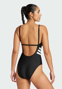 Maillot de bain une pièce noir avec bretelles réglables, dos ouvert et détail en rayure blanche sur le côté gauche. Texture lisse et mate.