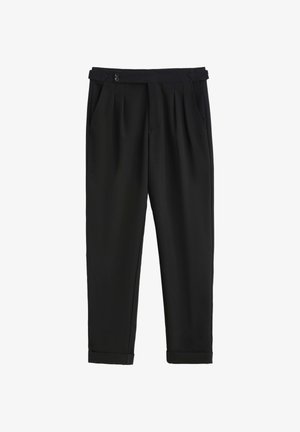 Pantalon noir en tissu lisse, avec un devant plissé, deux boutons à la taille et une jambe fuselée se terminant par des revers roulés.