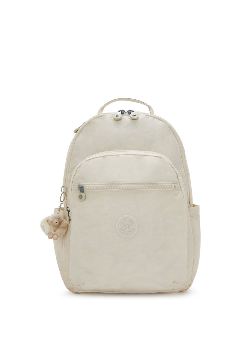 Mochila beige con forma redondeada, material de tela, cierre de doble cremallera, bolsillo frontal, bolsillo lateral y un llavero de mono esponjoso adjunto.