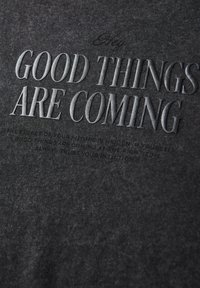 Dark gray cotton fabric featuring embossed text. The prominent slogan reads "GOOD THINGS ARE COMING," with smaller text underneath.