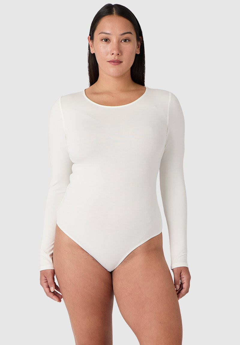 Långärmad vit bodysuit med rundad halsringning, slätt tyg och en figurnära design som smalnar av till en högskuren benöppning.