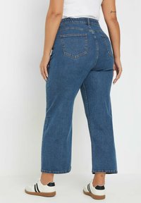 Blauwe wijdvallende denimjeans met een hoge taille, voorzien van achterzakken en uitgerafelde zoom, gedragen met witte sneakers met zwarte accenten.