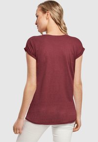 Bordeaux kortærmet t-shirt med rullede manchetter, blødt stof, buet kant og løs pasform. Blev båret med hvide bukser.
