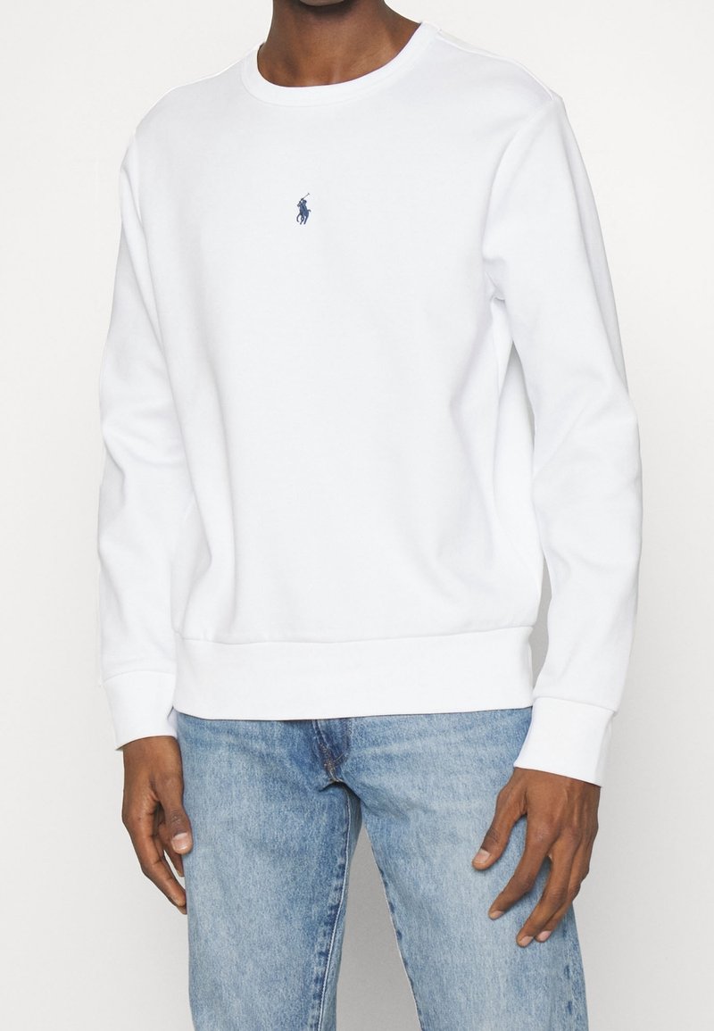 Biała bawełniana bluza z okrągłym dekoltem i długimi rękawami. Z przodu małe granatowe logo oraz ściągacze na mankietach i dole bluzy.