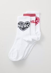 Hvide sokker med et sort og rødt hjerte-design og ordet "HUGO" i fed skrift. Blødt stof med ribbede bærestykker.