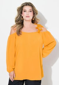 Gelbe, schulterfreie Bluse mit langen Ärmeln. Verfügt über florale Stickereien auf der linken Schulter. Weicher, leichter Stoff. Lockere Passform.
