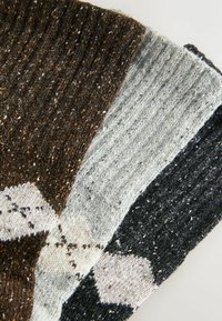 Stickad halsduk med en blandning av bruna, grå och svarta färger, med en ribbad textur och geometriskt mönster i ljusare nyanser.