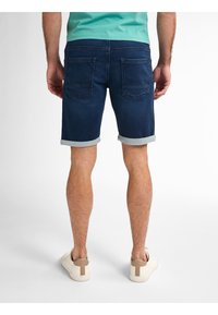 Shorts in denim blu scuro con risvolti, dotati di due tasche posteriori, abbinati a sneaker chiare. Tessuto morbido e testurizzato.