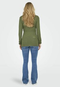 Olijfgroene gebreide sweater met lange mouwen, gecombineerd met lichtblauwe flared jeans. De sweater heeft een eenvoudig ontwerp met een rechte snit.