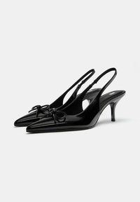 Čierne lakované džentlmenky s úzkymi špicatými špičkami, obsahujúce malú mašľu na priehlavku a tenký podpätok.