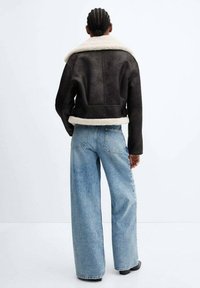 Sort læderjakke med shearling-fôr, bred krave og justerbare sidebånd, parret med lyseblå vide jeans.