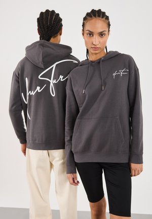 Two people with braided hair wearing gray hoodies with white script text, one facing front and one showing the back.