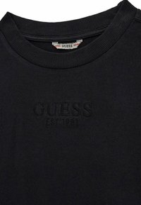 T-shirt in cotone nero con collo rotondo a coste e logo in rilievo "GUESS EST.1981" sul davanti. Texture liscia, design casual.