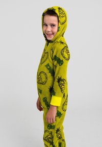 Tuta intera in pile verde con cappuccio, decorata con volti del Grinch e scritte, con polsini gialli su maniche e caviglie. Tessuto morbido.