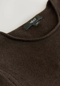 Brun sweater med en blød, tekstureret overflade og en rund halsudskæring. Har et sort label med "NEXT" i hvid tekst.