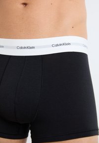 Zwarte katoenen boxershorts met een witte tailleband waarop het logo "Calvin Klein" in een herhaald patroon staat. Glad materiaal en een aansluitend ontwerp.