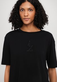 Black short-sleeve t-shirt in soft fabric featuring a raised logo design with the initials "AX" and "ARMANI EXCHANGE" printed below.