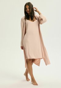 Jasnoróżowa sukienka z dekoltem w kształcie litery V i luźnym krojem, połączona z dopasowanym długim kardiganem, uszyta z miękkiego, zwiewnego materiału.