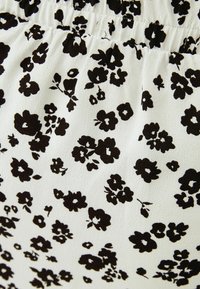 Svart blommönster på vit tyg, med olika blomstorlekar och former, med en slät textur och rynkade detaljer upptill.