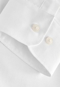 Colletto di camicia bianco con tessuto strutturato, due bottoni rotondi color crema e cuciture ordinate.