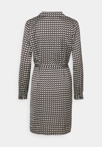 Svart och vit mönstrad klänning med långa ärmar, krage, midjebälte och geometrisk design av sammankopplade former över tyget.