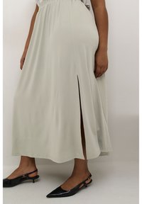 Light grey flowing maxi skirt with a side slit, made from soft fabric. Paired with black pointed-toe slingback shoes.