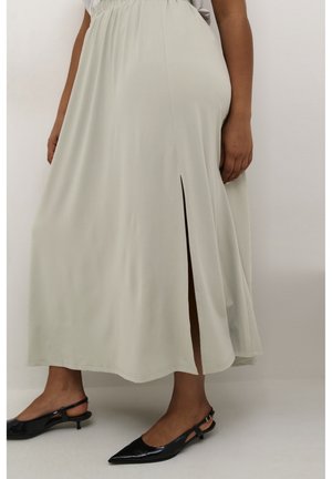 Light grey flowing maxi skirt with a side slit, made from soft fabric. Paired with black pointed-toe slingback shoes.