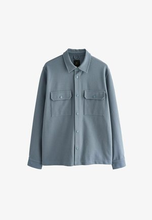 Světle modrá košile s dlouhým rukávem vyrobená z jemného materiálu, s límečkem, zapínáním na knoflíky a dvěma náprsními kapsami s klopami.