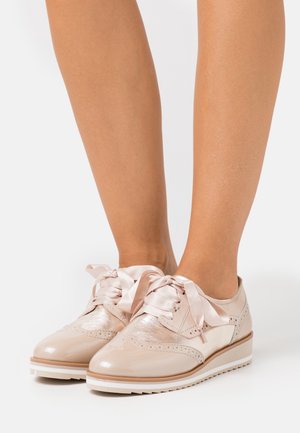 Scarpe in pelle verniciata beige pallido con lacci in raso, dettagli brogue e una suola bassa in gomma bianca.