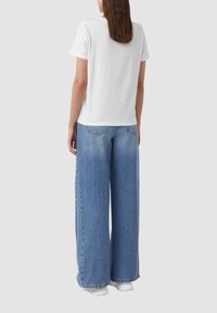 Weißes kurzärmliges T-Shirt kombiniert mit weit geschnittenen hellblauen Jeans, mit einem schlichten Design und lässiger Passform.