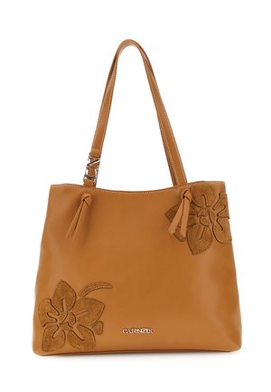 Brązowa skórzana torba typu tote z dwoma paskami na ramię, kwiatowymi aplikacjami z zamszu na rogach oraz małą metalową plakietką z logo na przodzie.