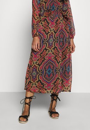 Langes, gemustertes Kleid mit langen Ärmeln in Schwarz-, Pink-, Blau- und Goldtönen. Es hat eine taillierte Taille und fließenden Stoff. Kombiniert mit schwarzen Sandalen.