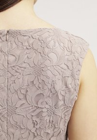 Gros plan sur le haut du dos d'une femme portant une robe sans manches en dentelle mauve avec des motifs floraux et une fermeture éclair au dos.