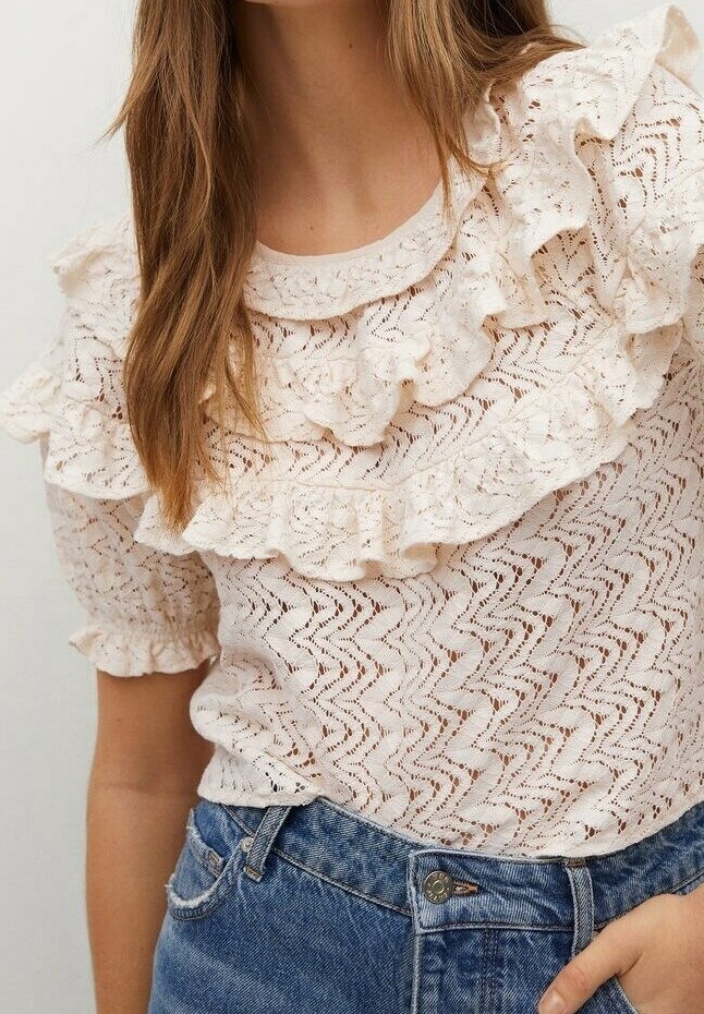 Haut beige clair avec un design texturé et froncé. Présente un motif en vagues et des manches courtes bouffantes, associé à un denim.