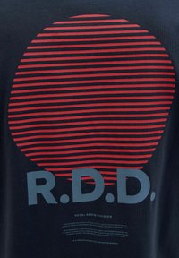 Navy krāsu T-krekls ar sarkaniem horizontāliem svītrainiem, veidojot apli. Iespiests teksts "R.D.D." pelēkā krāsā un papildu informācija zem tā.