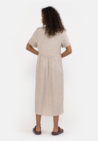 Abito midi beige con maniche corte, tessuto texturizzato, vita arricciata e vestibilità ampia. Indossato con calzature scure senza lacci.