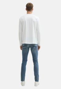 Camisa blanca de manga larga hecha de un tejido ligero, combinada con jeans azules ajustados. Los zapatos son blancos, con una textura suave y un diseño minimalista.