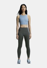 Un crop top bleu clair et un legging taille haute vert foncé avec une texture lisse, associés à des chaussures de sport grises avec des accents bleus.